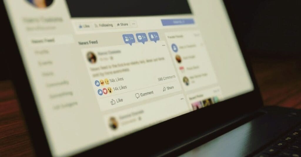 Close-up angle of a laptop monitor displaying a social media news feed interface with notification icons, likes, and comment counts.
