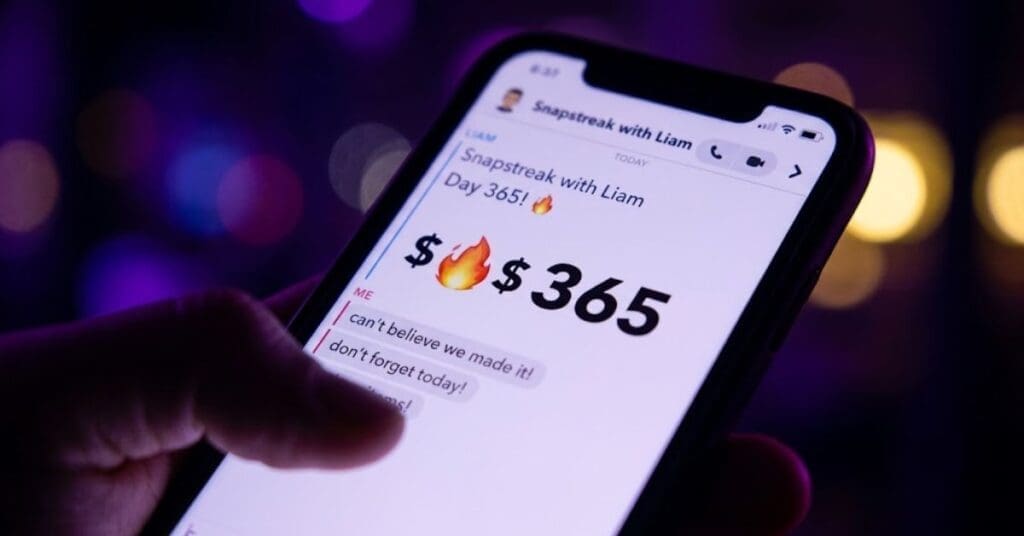 Close-up of a hand holding a smartphone displaying an urgent text message conversation with a high-number streak and fire icon, illuminated by artificial purple and yellow lights.