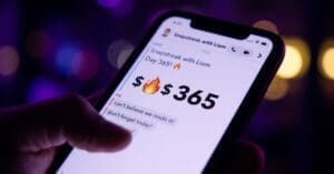 Close-up of a hand holding a smartphone displaying an urgent text message conversation with a high-number streak and fire icon, illuminated by artificial purple and yellow lights.